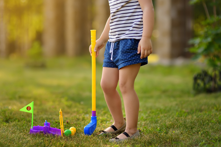 Little girl playing mini golf in spring park. Child having fun with active leisure on vacations